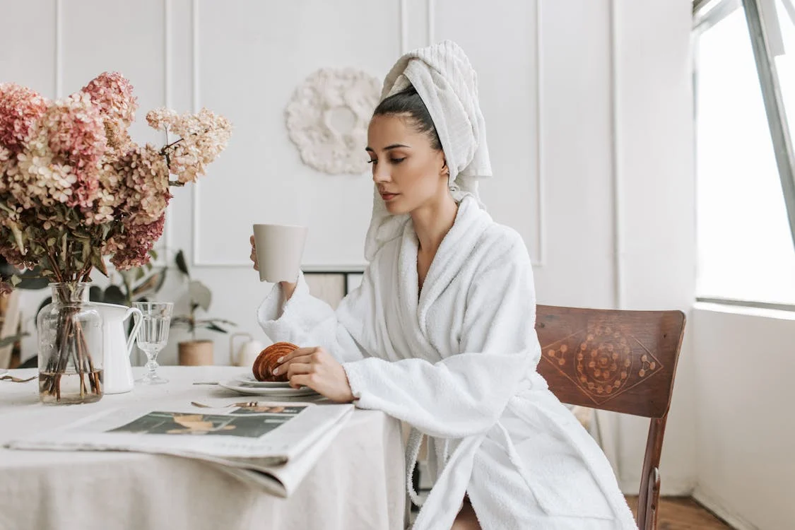 Geschenke zur Geburt: Was 6 Kulturen besser wissen 4 Junge Frau im Bademantel geniesst eine Tasse Tee — Selfcare-Geschenk fuer frischgebackene Muetter
