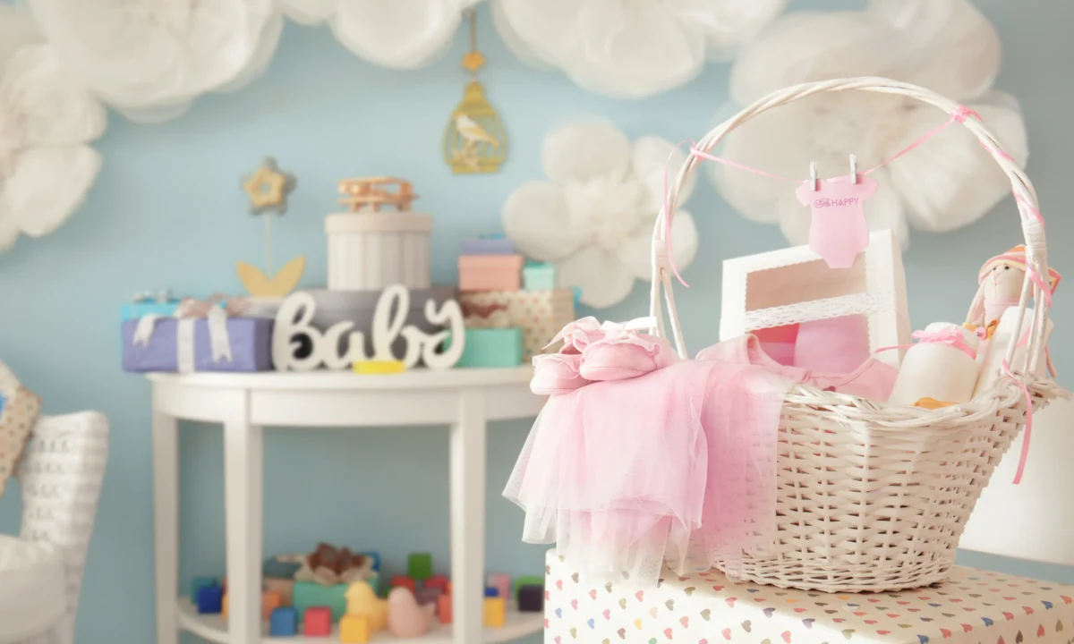Geschenkkorb zur Geburt mit rosa Babykleidung, Babyschuhen und Stoffpuppe — liebevoll dekoriert für eine Babyparty