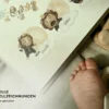 Aufgeschlagenes Babytagebuch mit Aquarell-Löwen-Illustrationen neben Babyfüßen und Holzspielzeug